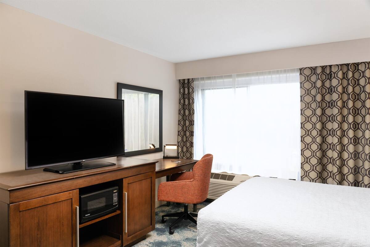 A hotel room with a bed, a desk with a flat-screen TV, a microwave, and a chair.