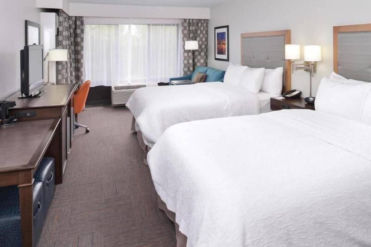 A hotel room with two beds, a desk, a chair, a television, and a window with curtains.