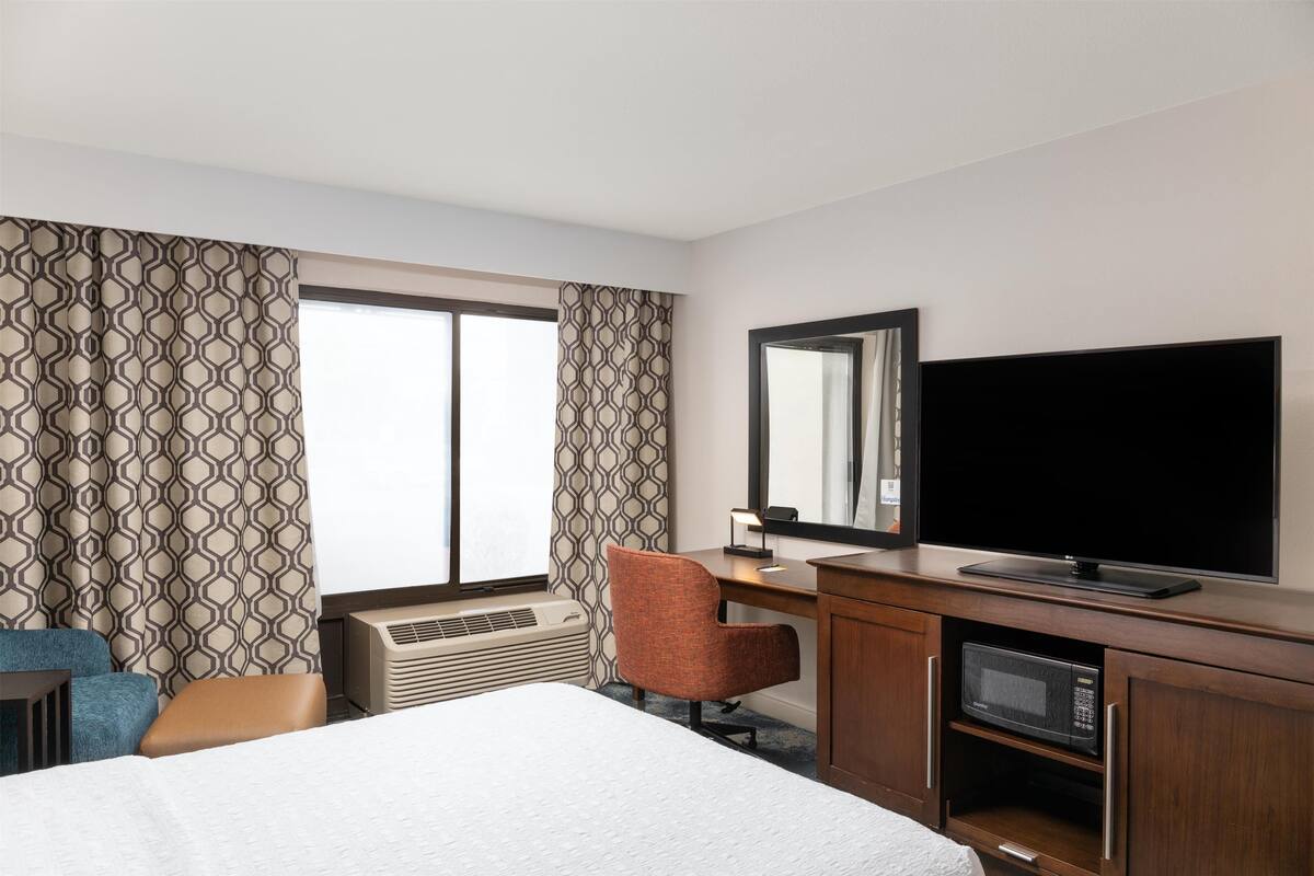 A hotel room with a bed, a desk with a flat-screen TV, a chair, and a microwave.