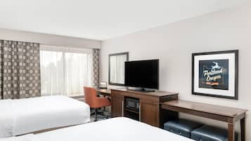 A hotel room with two beds, a desk with a television, a chair, and a framed picture on the wall.