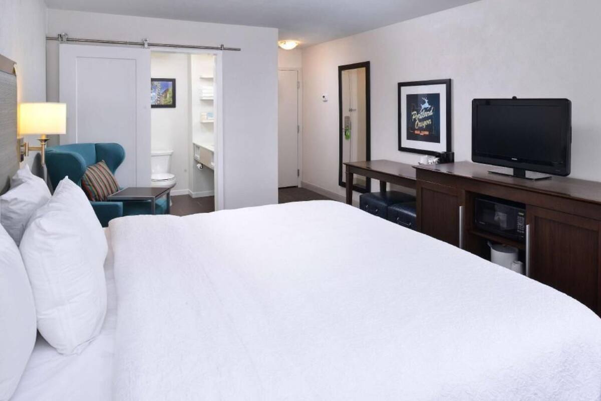 A hotel room with a bed, a desk, a television, and a bathroom visible through an open door.