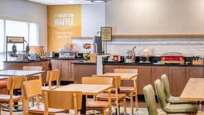 A restaurant with wooden tables and chairs, a kitchen area, and a sign reading "The Hampton Waffle".
