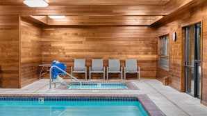 A wooden-paneled indoor pool area with a blue-tiled pool, four grey chairs, and a blue water slide.