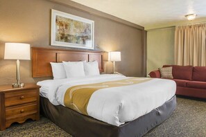 A hotel room with a large bed, two bedside lamps, a red sofa, a framed artwork above the bed, and a patterned carpet. - Quality Inn University Center (Pittsburgh)