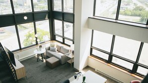 Une pièce spacieuse avec de grandes fenêtres, un canapé, une table à manger et une petite table ronde avec une lampe.
