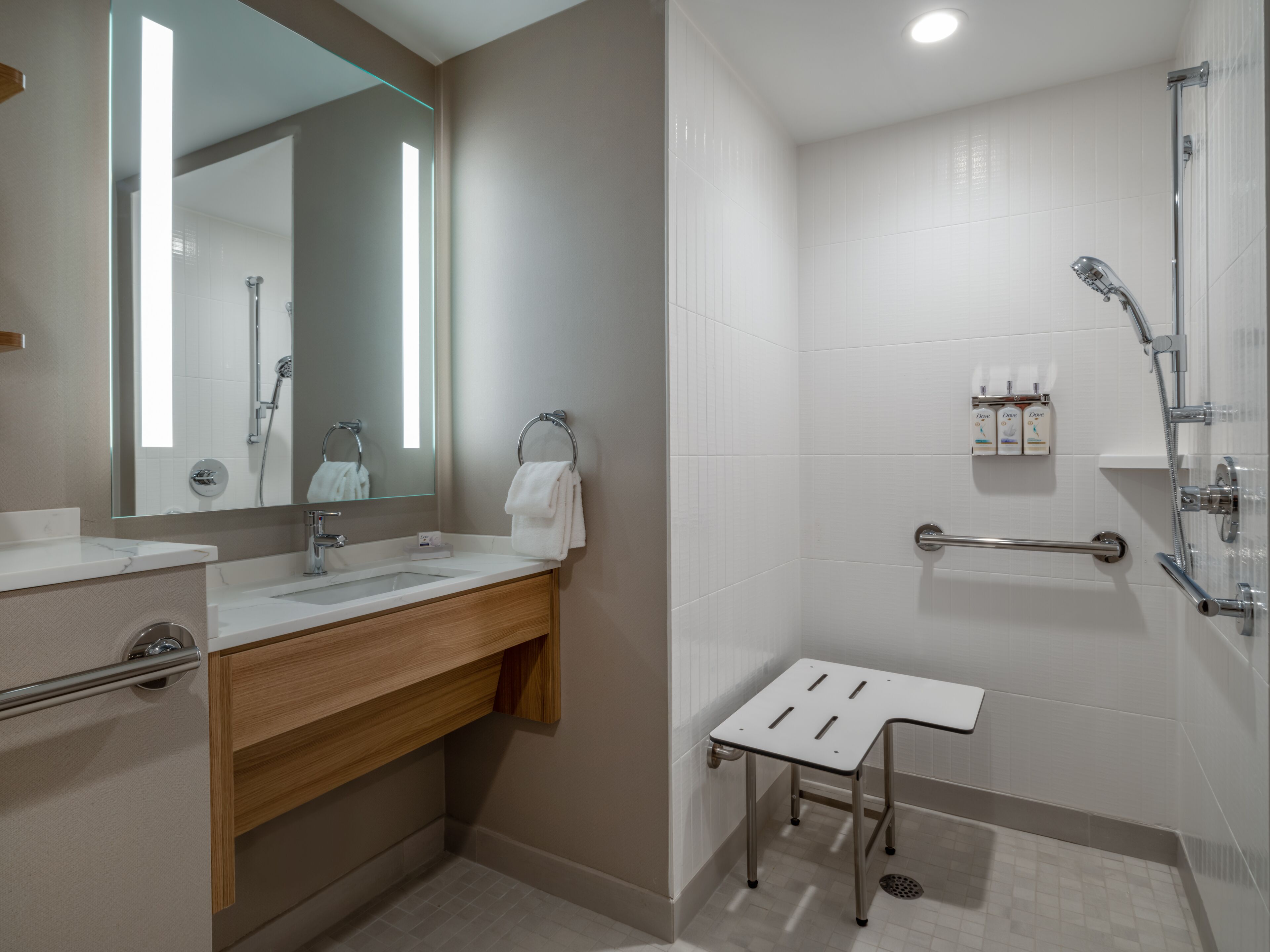 A modern bathroom with a sink, mirror, towel rack, shower, and a small table.