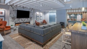 Un espace de détente moderne comprenant un canapé d’angle, une cheminée et un bar avec des tabourets.