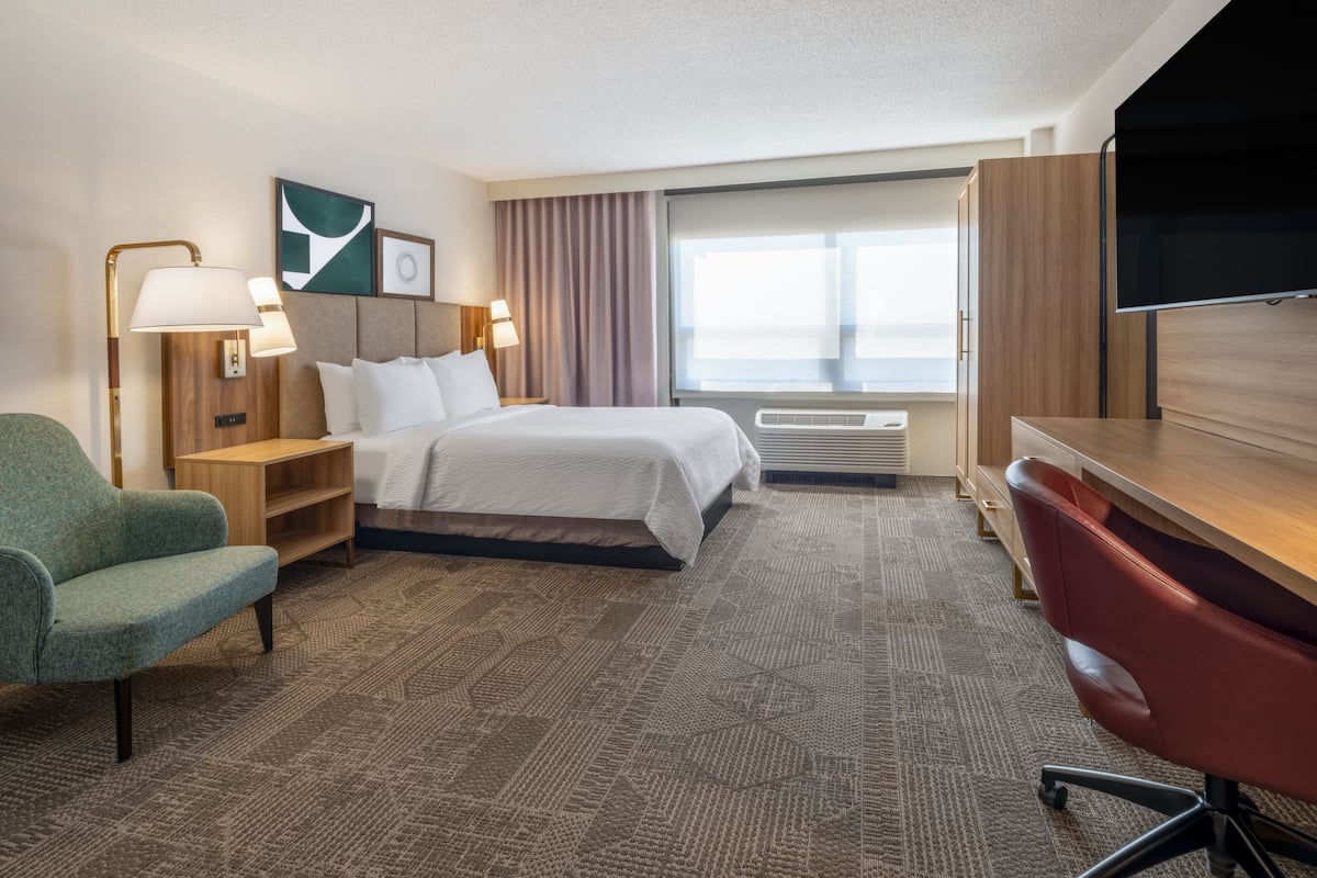 Une chambre d’hôtel équipée d’un lit, d’un bureau, d’une chaise, d’une télévision, d’une lampe et d’une fenêtre avec des rideaux.