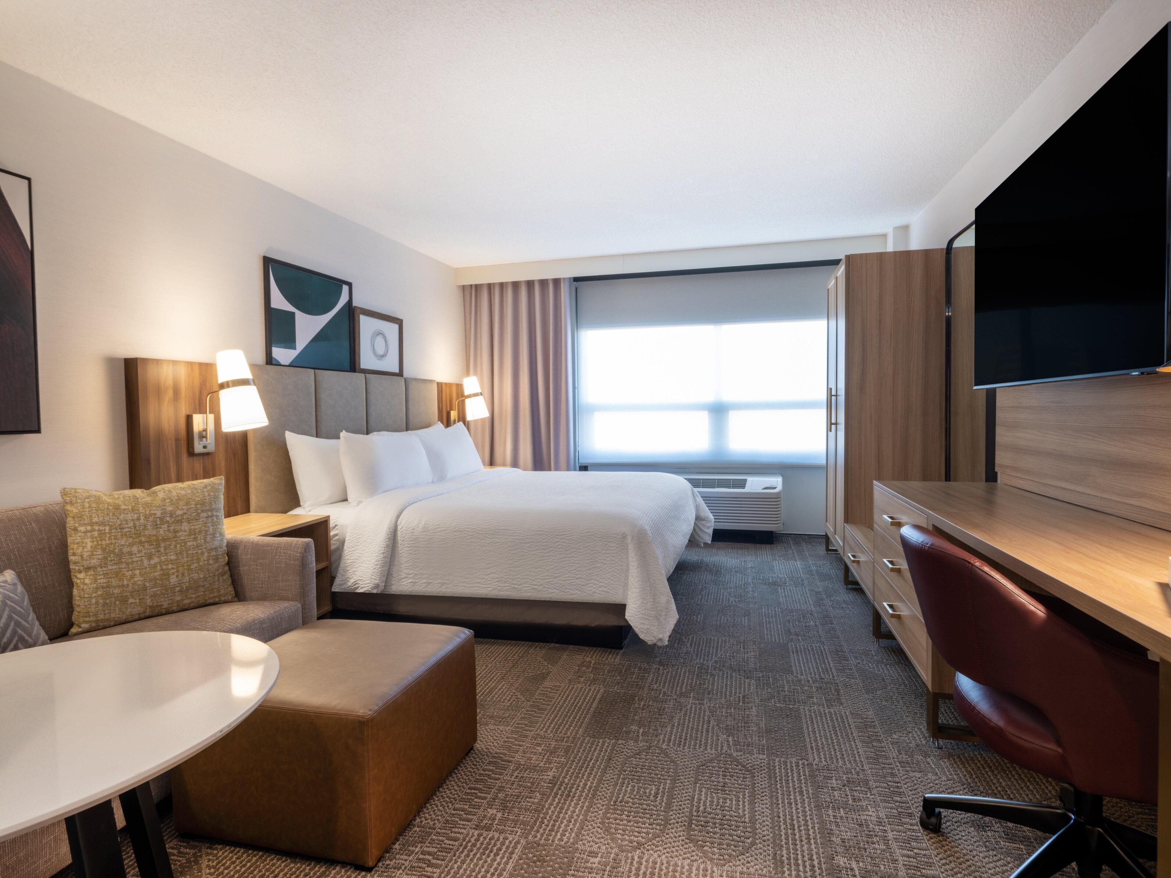Une chambre d’hôtel équipée d’un lit, d’un bureau, d’une chaise, d’une télévision et d’une fenêtre avec des rideaux.