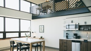 Une cuisine moderne avec un coin repas, de grandes fenêtres et un escalier menant à l’étage supérieur.