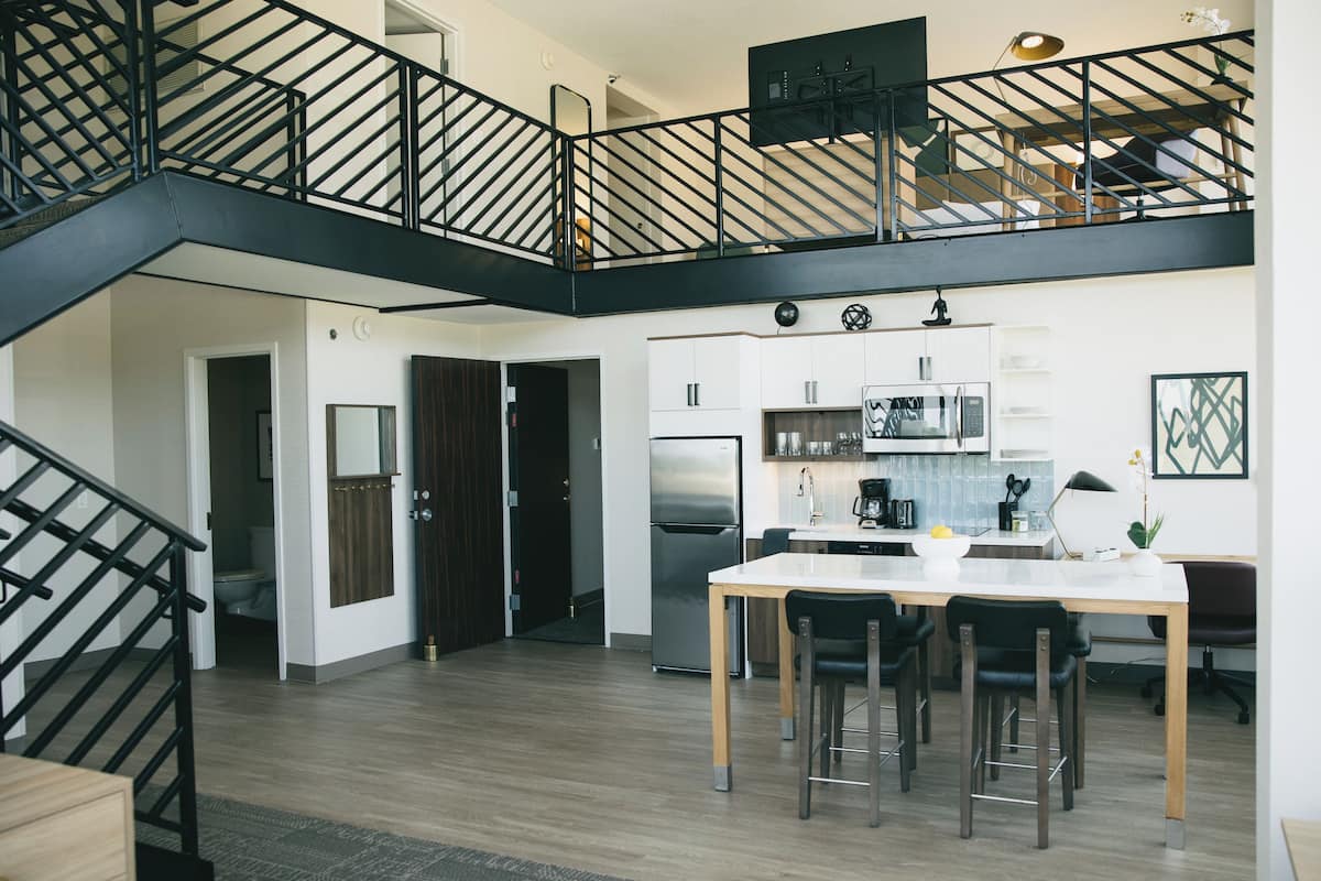 Une cuisine moderne dotée d’un îlot central, d’un coin repas avec une table et des chaises, et d’un escalier menant à un niveau supérieur.