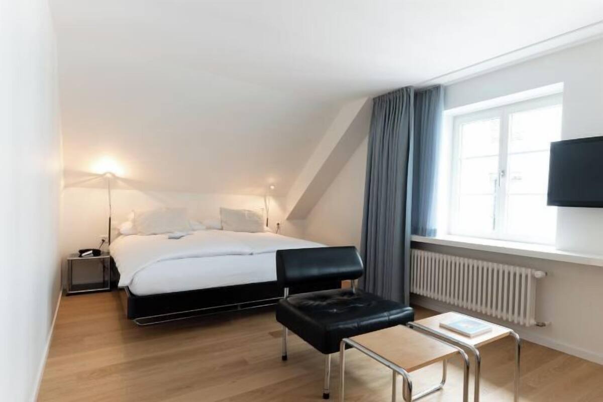 Un dormitorio con cama, mesita de noche, lámpara y televisor en la pared.