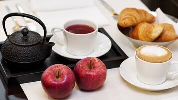 A breakfast tray with a teapot, cups of tea and coffee, apples, croissants, and a fork.