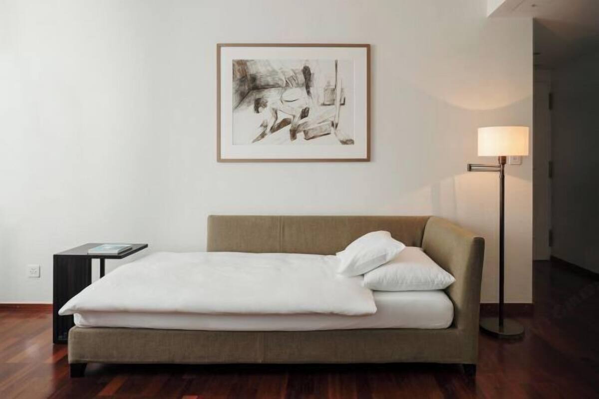Un dormitorio con una cama, un cuadro abstracto enmarcado, una mesita de noche y una lámpara de pie.