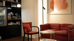 A modern living room with a red leather sofa, a black chair, a small round table, and a bookshelf filled with books and decorative items. - Boutique Hotel Helmhaus Zurich (Zürich)