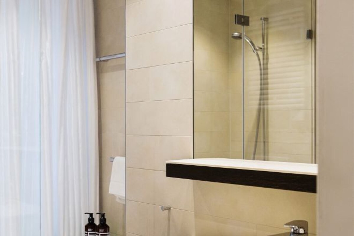 A modern bathroom with a glass-enclosed shower, a white sink with a black countertop, and a towel hanging on the wall.
