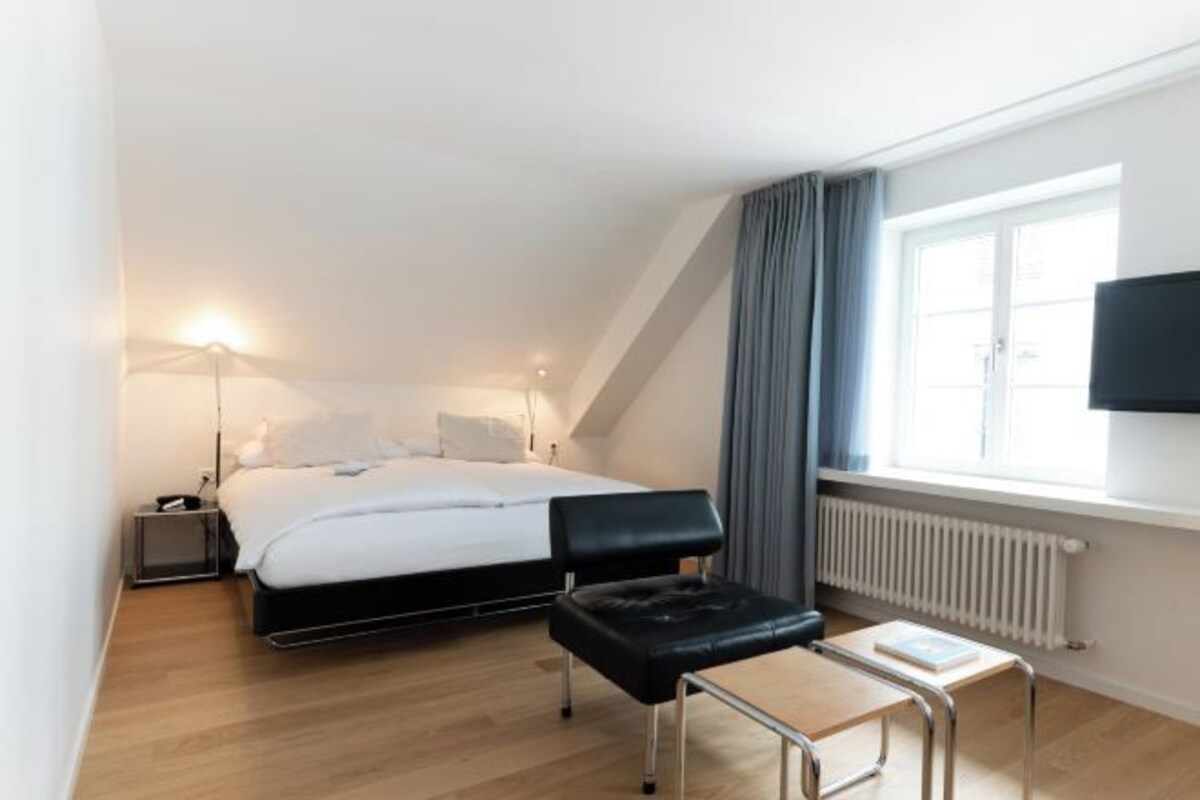 A bedroom with a bed, bedside table, lamp, and a TV on the wall.