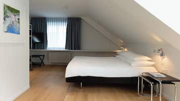 A modern bedroom with a bed, a desk, a chair, a radiator, and a painting on the wall.