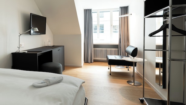 A modern hotel room with a bed, desk, chair, and wardrobe. - Boutique Hotel Helmhaus Zurich (Zürich)