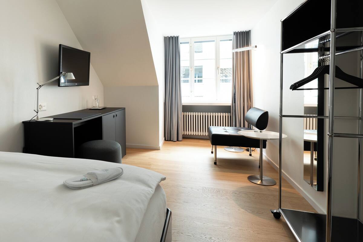 A modern hotel room with a bed, desk, chair, and wardrobe.