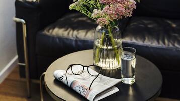 Un tavolino rotondo con un giornale, un paio di occhiali, un bicchiere d'acqua e un vaso con fiori.