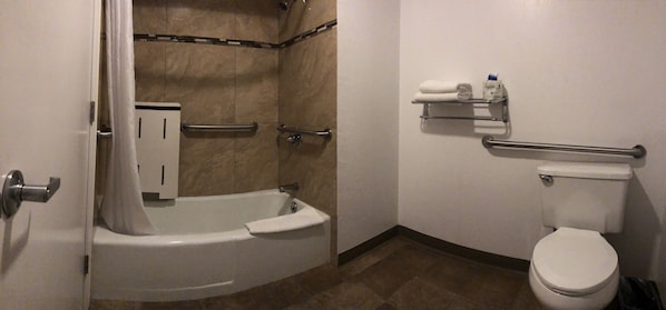 Bathroom features a bathtub, toilet with grab bar, and shelf for toiletries.