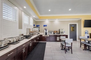A modern kitchen with a long counter, microwave, coffee machine, and a water dispenser. There are chairs and tables for dining, and a TV mounted on the wall. - Best Western Inn Santa Clara (Santa Clara)