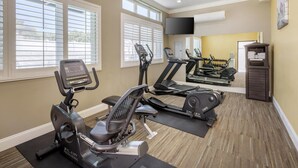 Ein Fitnessstudio mit Trainingsgeräten, großen Fenstern und einem Flachbildfernseher.
