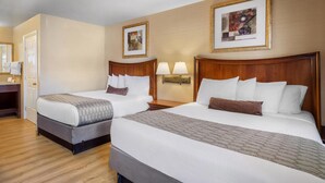 Ein Hotelzimmer mit zwei Betten, einem Holzkopfende, einem Nachttisch, einer Lampe und einem gerahmten Bild an der Wand.