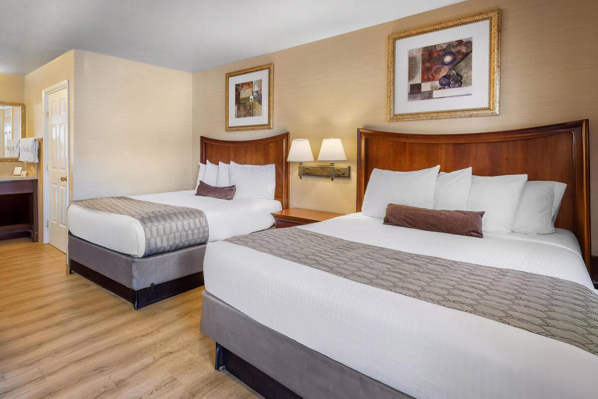 A hotel room with two beds, a wooden headboard, a nightstand, a lamp, and a framed picture on the wall.