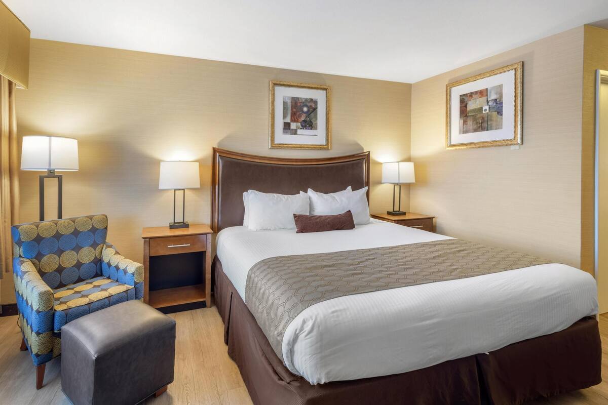 A hotel room with a large bed, two bedside tables, a chair, and a footstool.