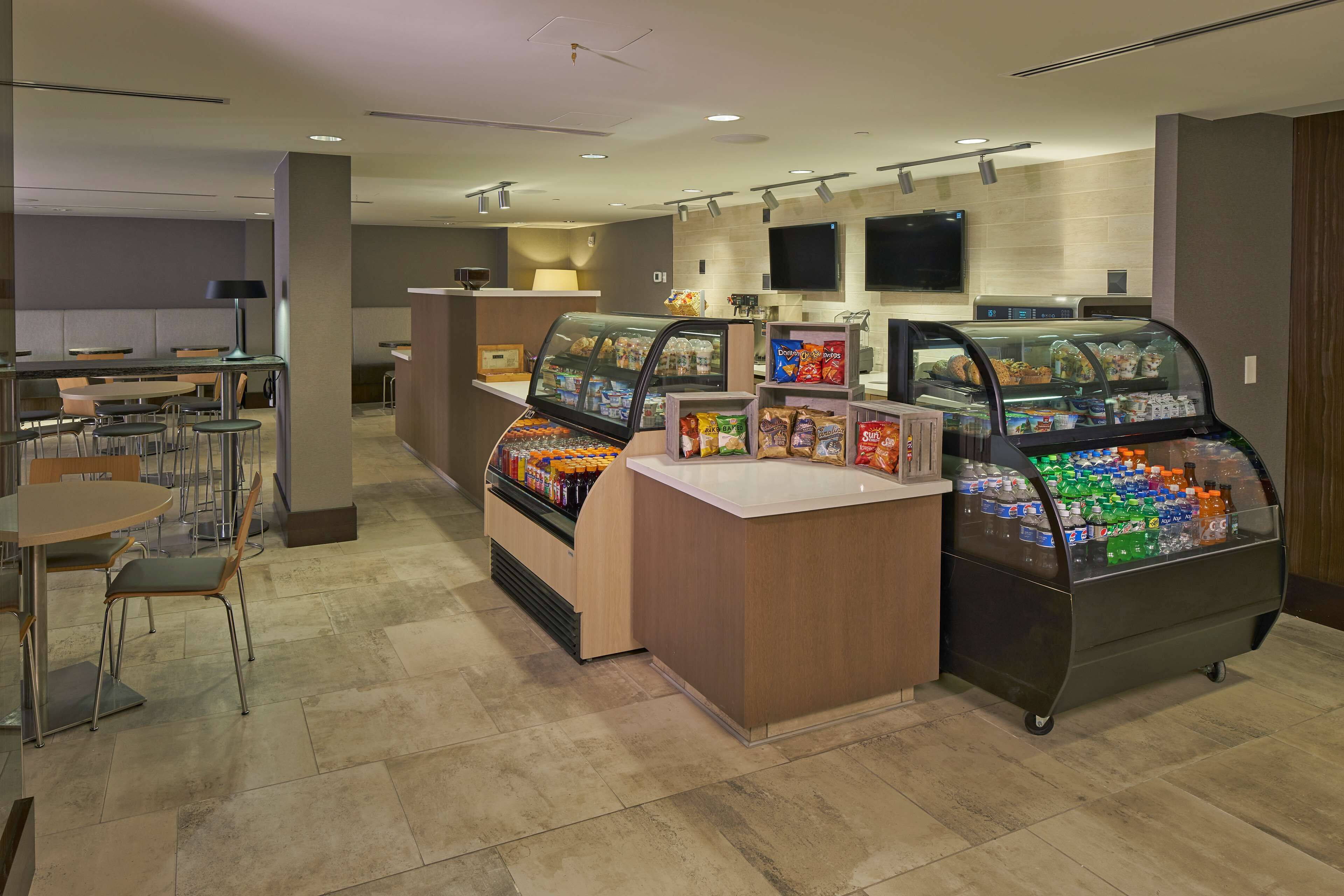 A modern cafe with seating, a counter, and refrigerated display cases with snacks and drinks.