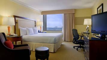 Habitación de hotel con una cama grande, un escritorio con computadora, una silla, un taburete pequeño y un televisor.