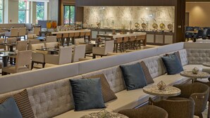 Un hall d’hôtel spacieux, doté de plusieurs espaces de détente, notamment un long banc agrémenté de coussins, des tables rondes et un bar avec un comptoir en marbre.