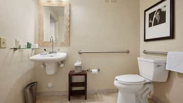 A bathroom with a sink, mirror, toilet, and a small trash bin.