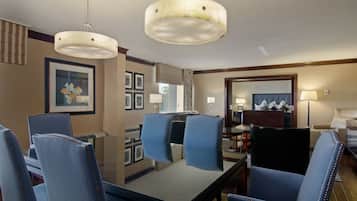 Ein Hotelzimmer mit Essbereich, ausgestattet mit einem Glastisch und blauen Polsterstühlen, einem großen Spiegel und einer Kristallleuchtreiter.
