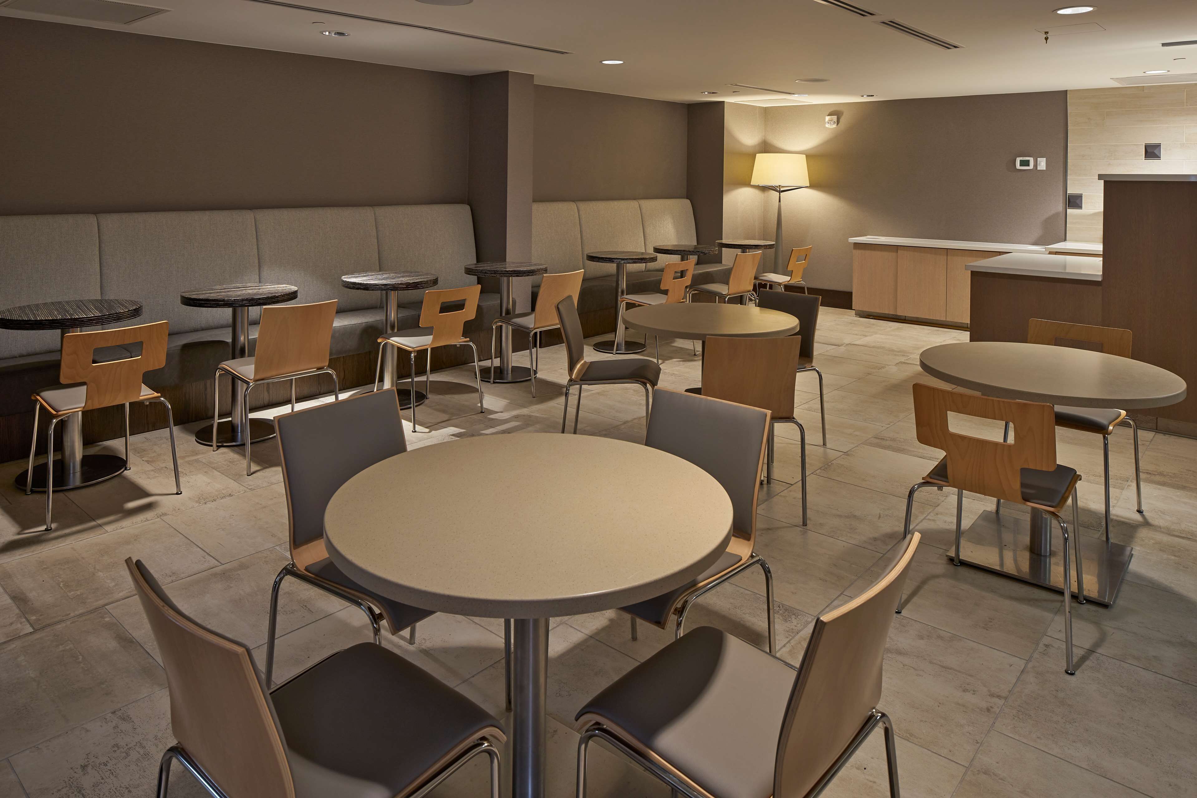 A hotel lobby with multiple seating areas including round tables and sofas, a reception desk, and a lamp.
