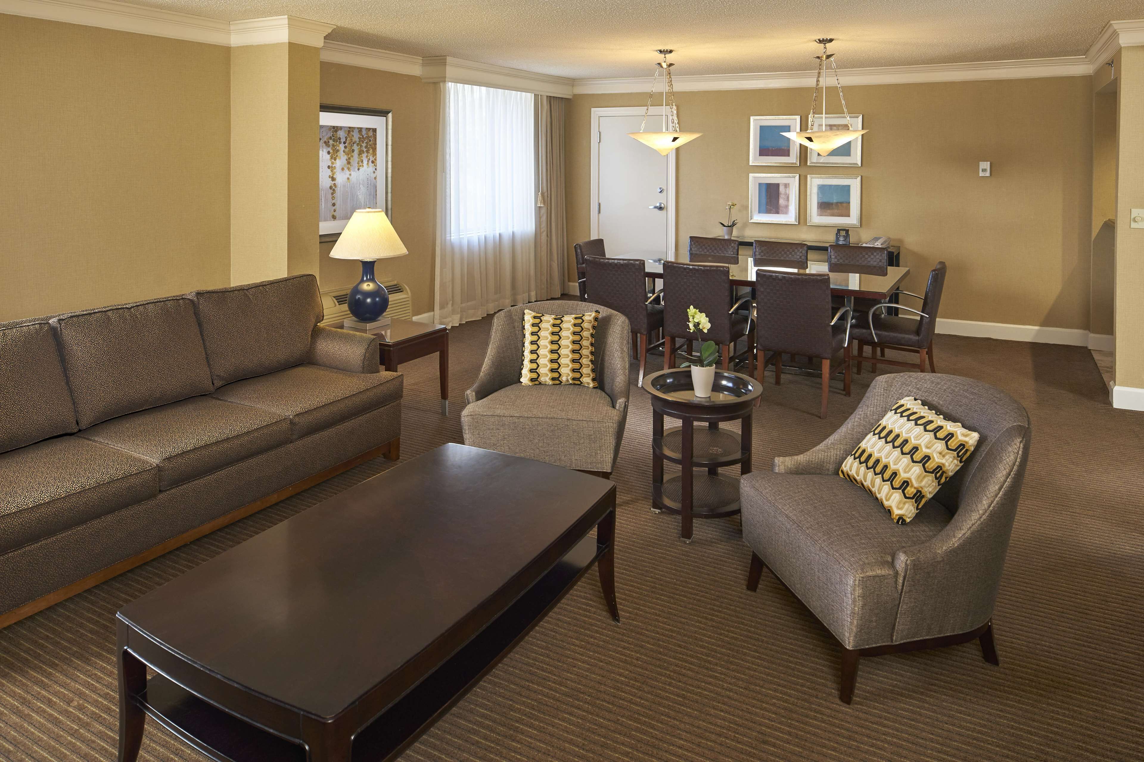 Quarto de hotel com sofá, poltronas, mesa de centro, mesa de jantar e cadeiras, e um candelabro.