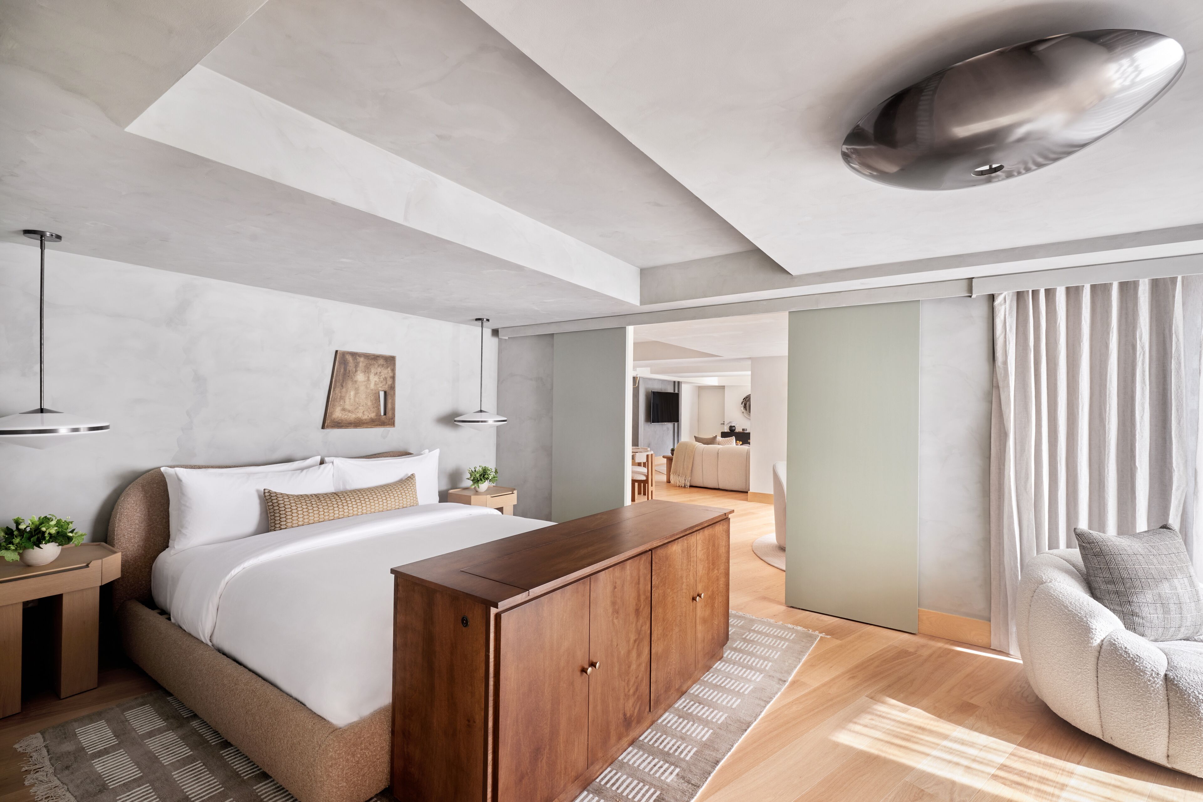 A modern bedroom with a large bed, wooden wardrobe, and a view of the living area.
