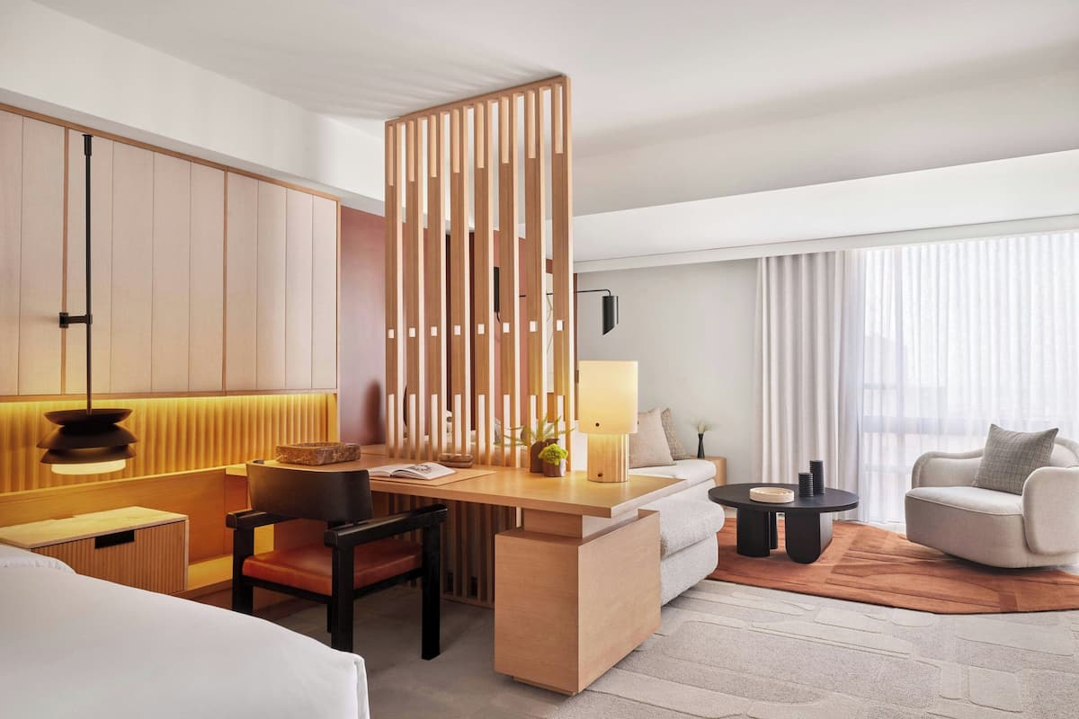 A hotel room with a wooden partition, a desk with a lamp, a sofa, a chair, and a bed.