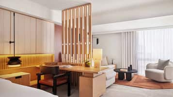 A hotel room with a wooden partition, a desk with a lamp, a sofa, a chair, and a bed.