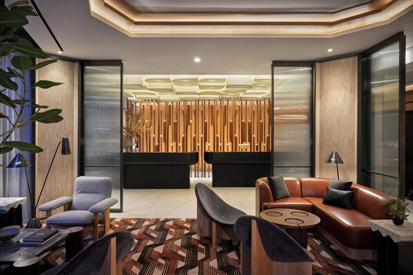 A modern lobby with a curved ceiling, a seating area with a brown leather sofa and grey armchairs, and a patterned floor. - The Jay, Autograph Collection (San Francisco)