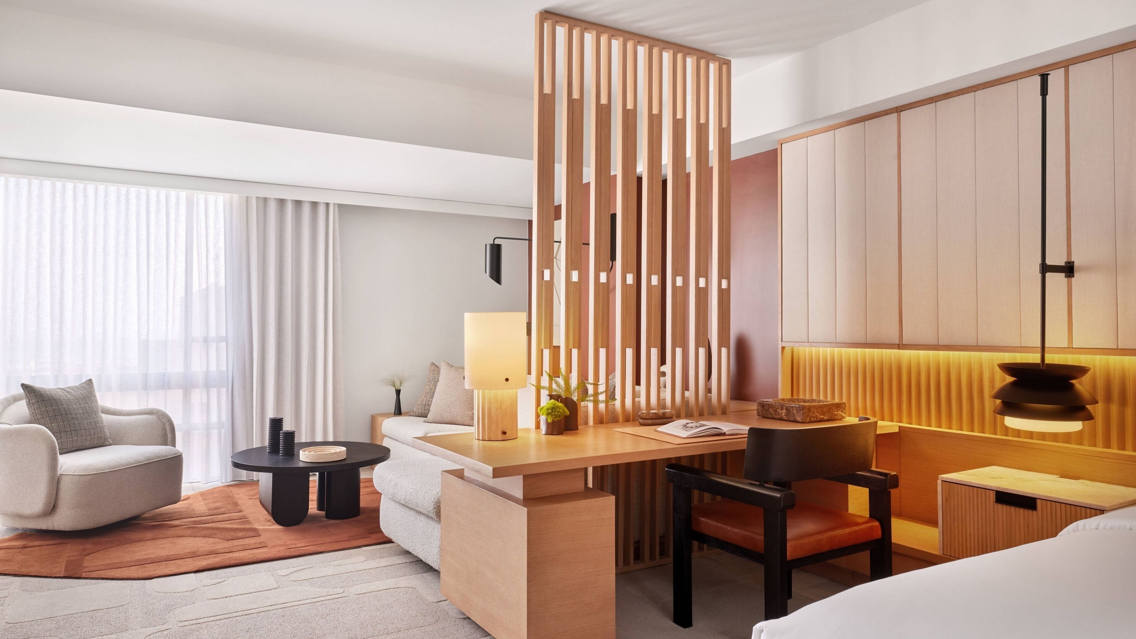 Ein modernes Hotelzimmer mit einer Sitzecke, einem kleinen Schreibtisch, einem Sessel, einem Bett und einer Holzwand.