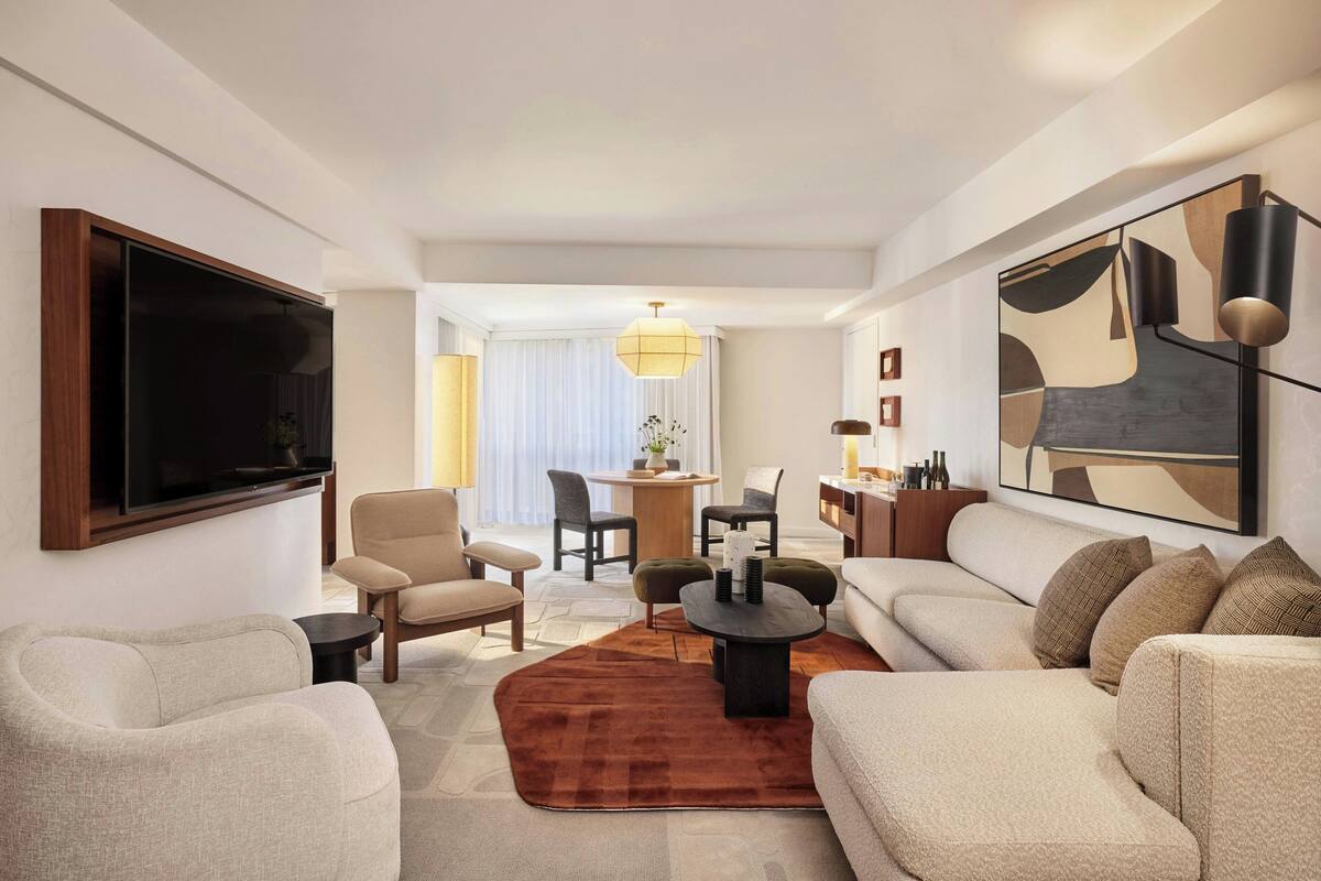A modern living room with a flat-screen TV, beige sofas, a coffee table, and a dining area with a chandelier.