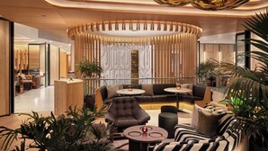 A modern lobby with a central seating area, a reception desk, and a decorative wooden panel. - The Jay, Autograph Collection (San Francisco)
