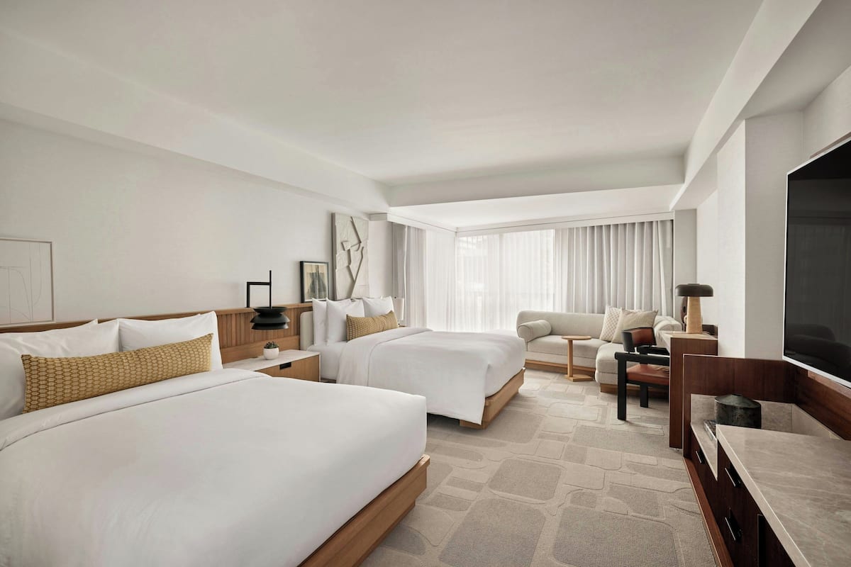 A hotel room with two beds, a sofa, a TV, and a large window with curtains.