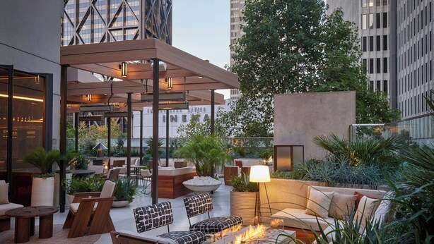 A rooftop lounge with outdoor seating, a fire feature, and a view of a cinema in the background. - The Jay, Autograph Collection (San Francisco)