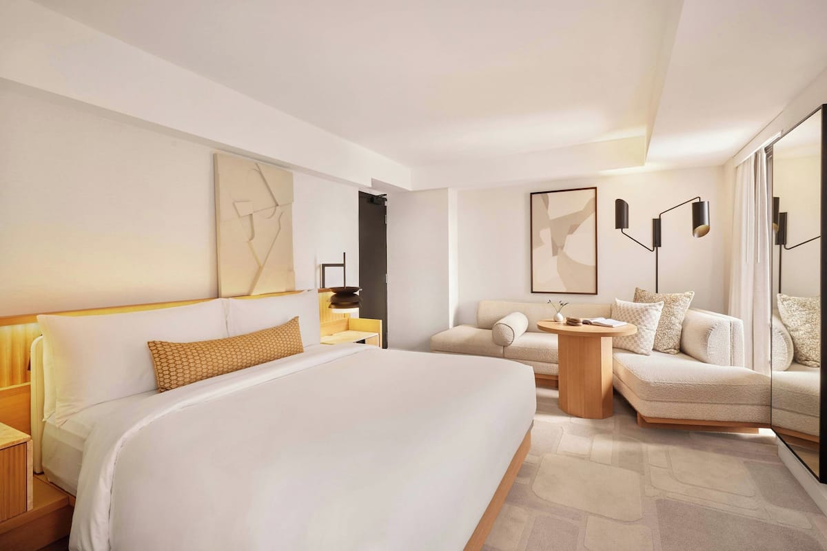 A modern hotel room with a large bed, a sofa, a small table, and a mirror.