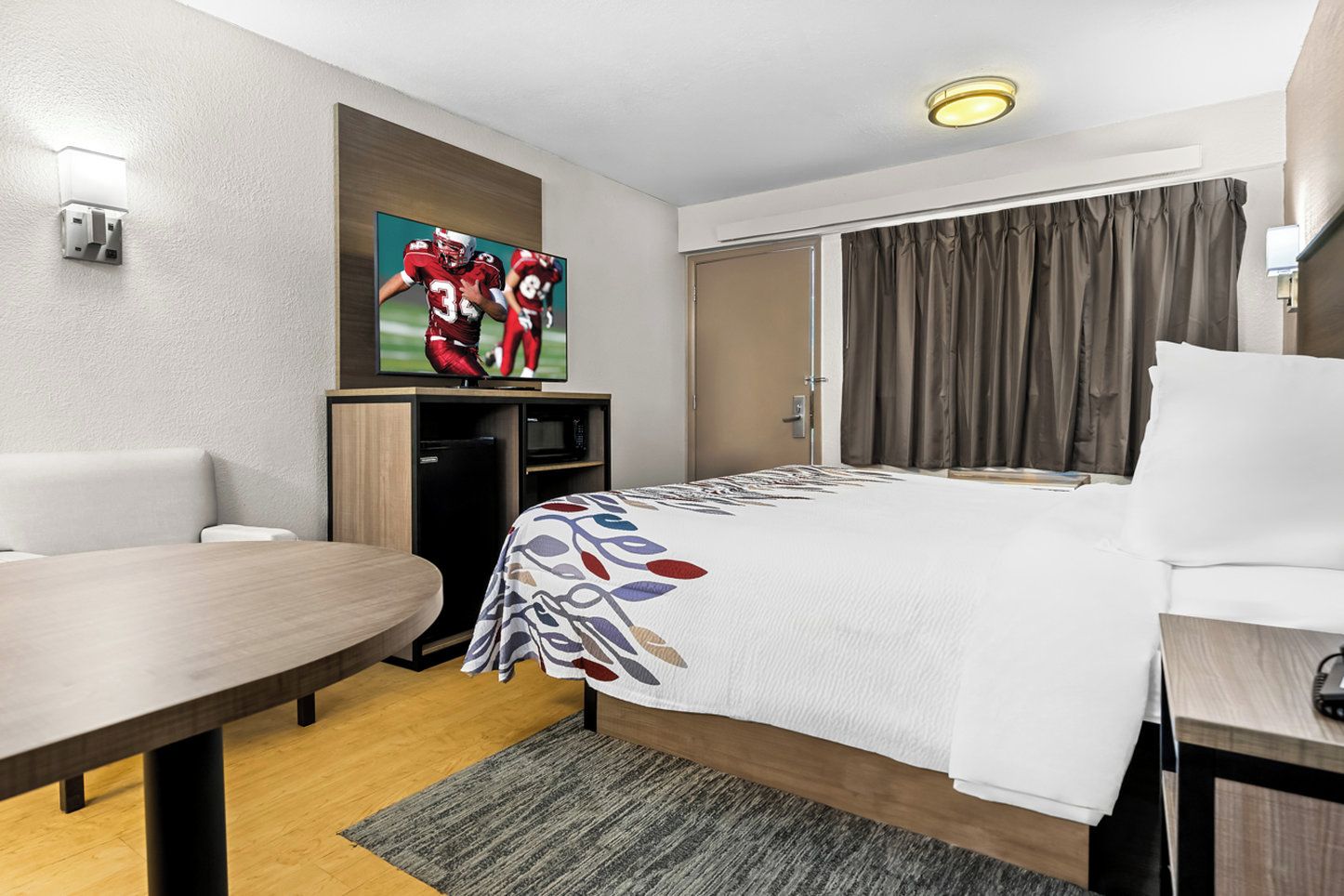 A hotel room with a bed, a desk, a television mounted on the wall, and a door.