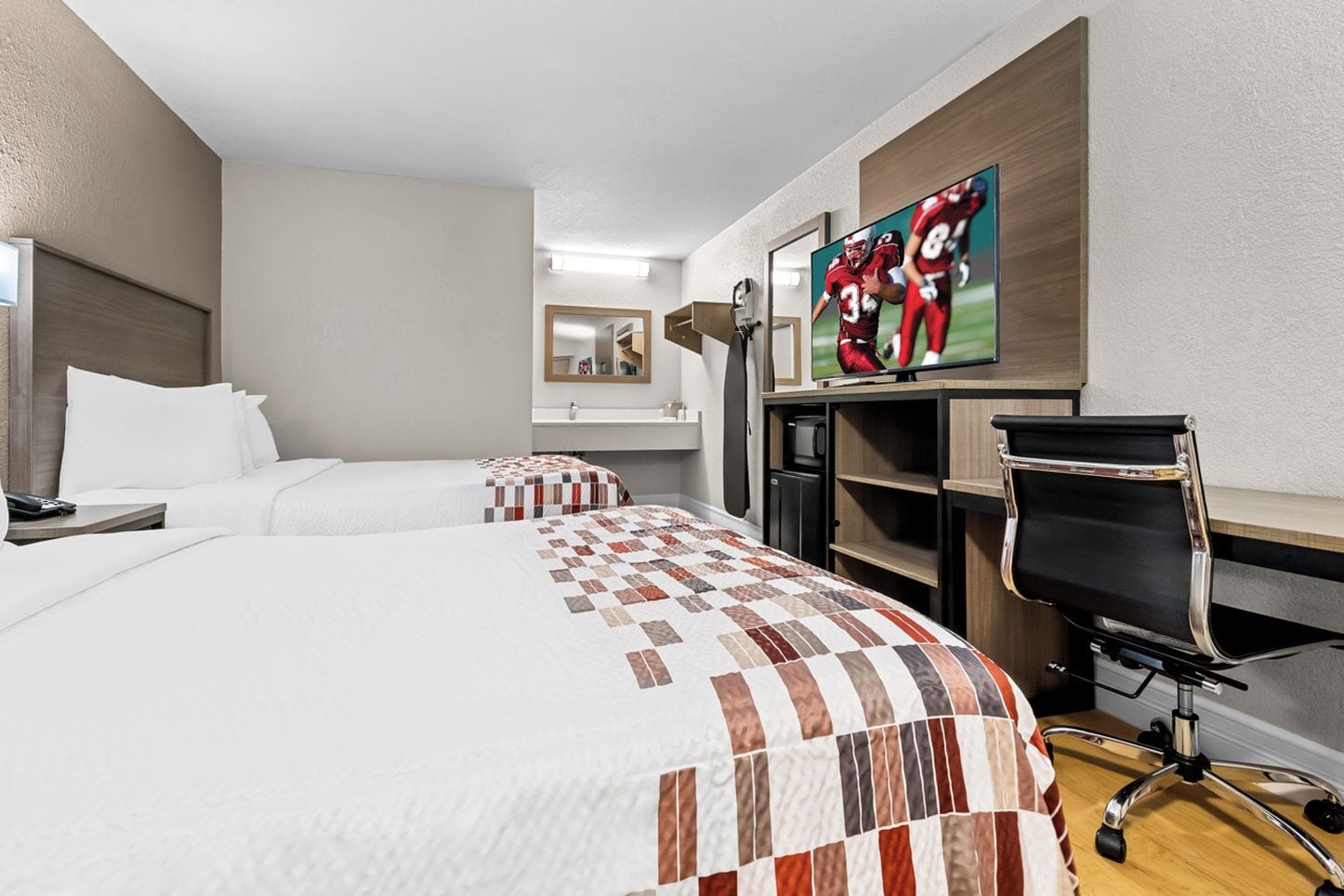 A hotel room with two beds, a desk, a chair, a TV, and a painting on the wall.